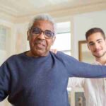 Elderly man smiling with caregiver in a supportive home environment, promoting health and happiness., tags: startet für - pexel