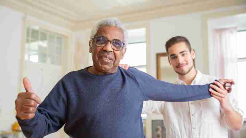 Elderly man smiling with caregiver in a supportive home environment, promoting health and happiness., tags: startet für - pexel